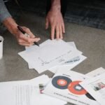 Two people collaborate during a business meeting, writing notes on papers with coffee cups nearby.